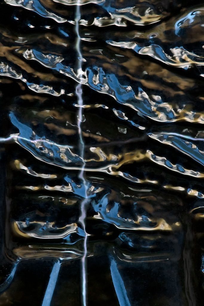 "Liquidized": Close-up macro photograph of glass in fluid tones of blue, golden-brown, and black, evoking a sense of motion and liquidity.