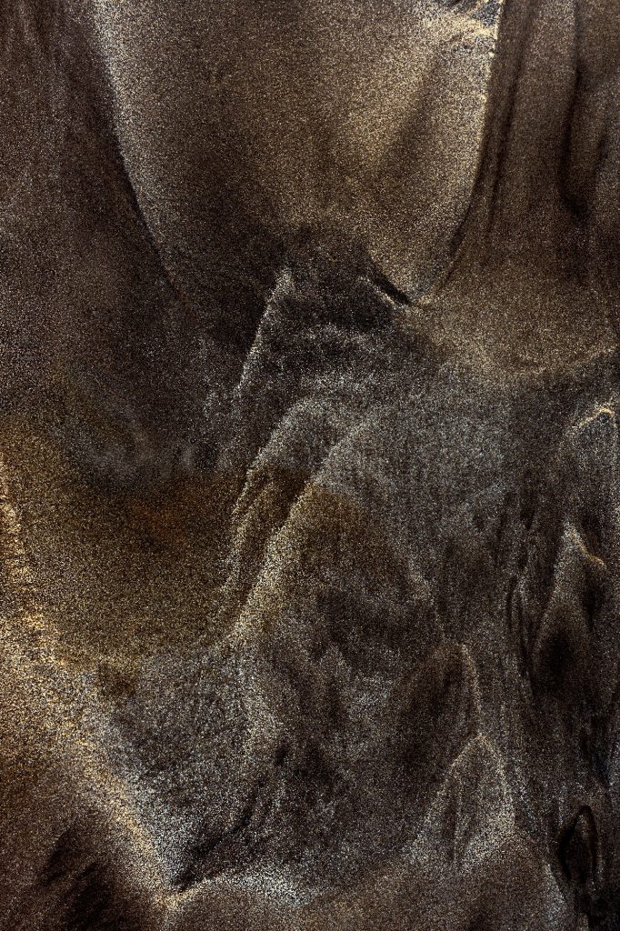 "Wrafts of Mist": Abstract close-up photograph depicting swirling patterns in a mixture of volcanic black sand and white beach sand on the shores of Bali, Indonesia. Evokes the transient beauty of mist flowing around mountain ranges.