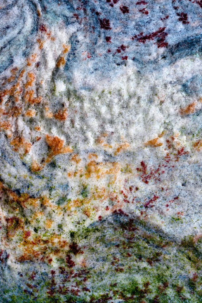 Individual red leaves swirl in the air against a calm, stony backdrop.