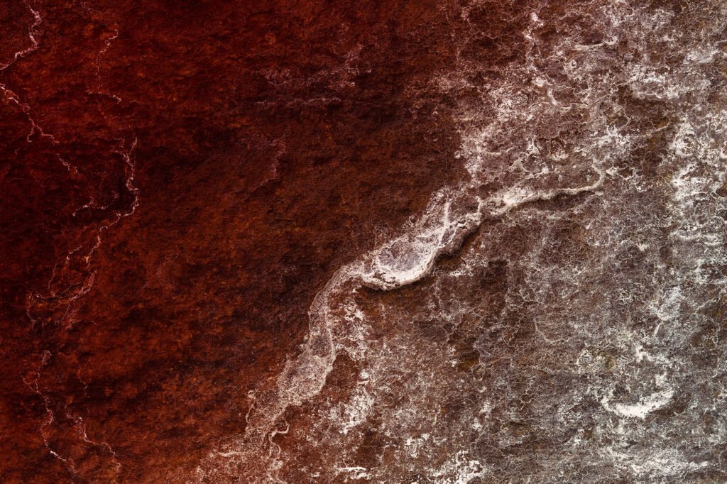 Rust-red iron stains and pale lime traces on dark basalt stone – frozen ripples drawn across the weathered surface of an old bridge.
