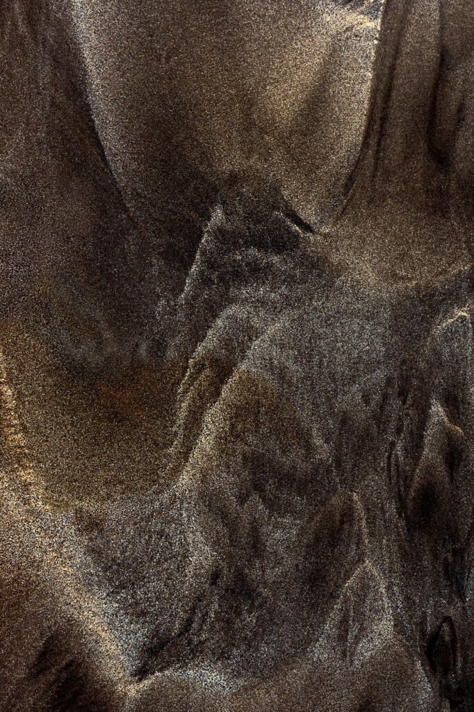 Basalt dust and sand form black and white granular patterns in a misty atmosphere — a fleeting volcanic moment on an island.